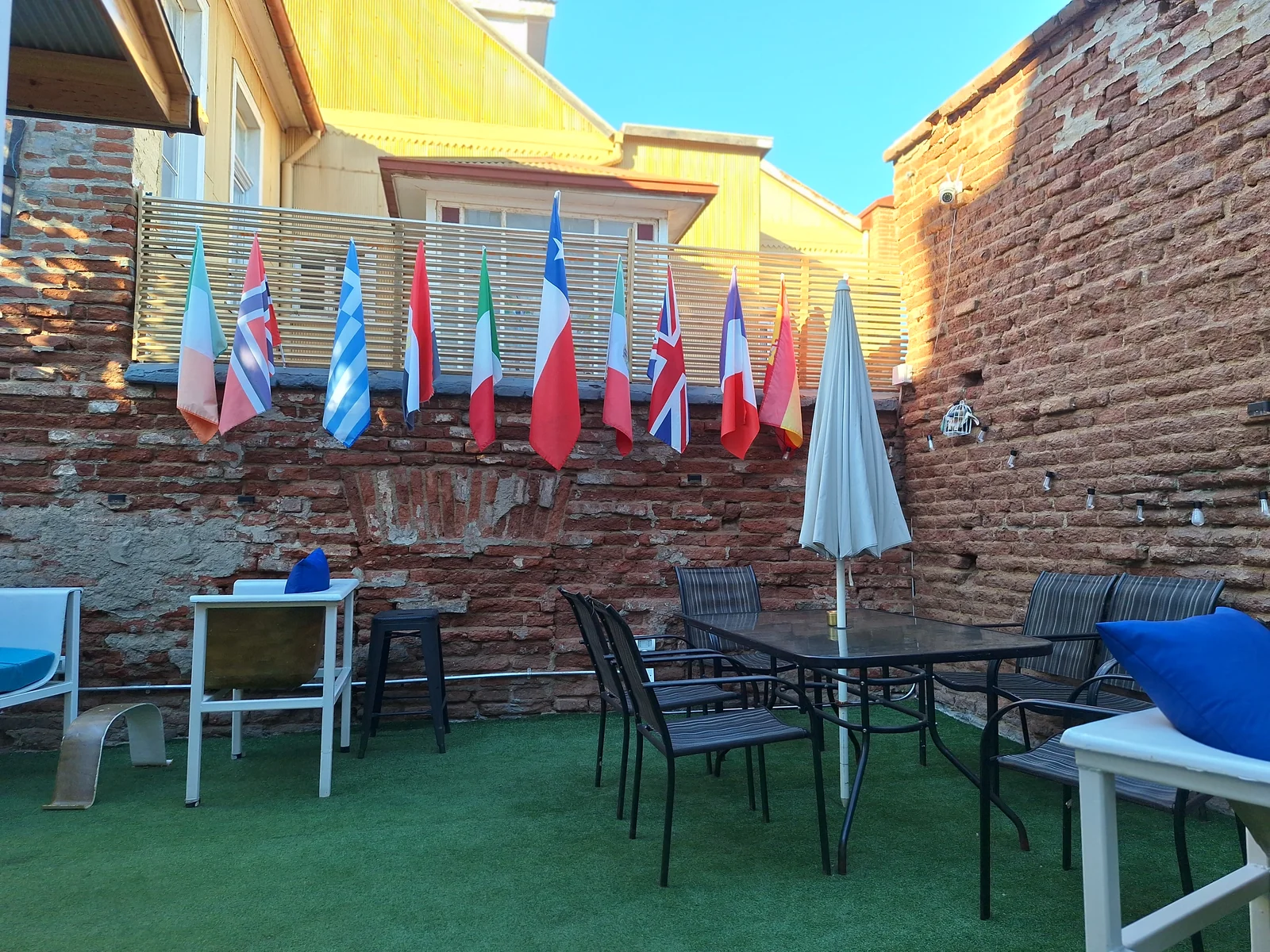 Patio trasero de CasaFran con banderas, mesas y sillones junto a muros de ladrillo